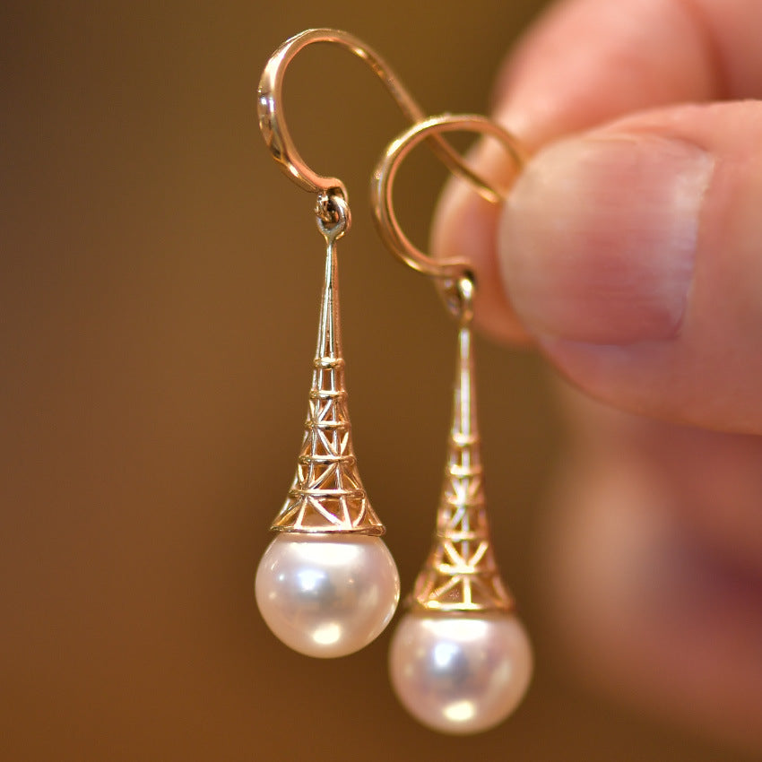 Gold earrings with pearl drops held by a hand against a blurred background