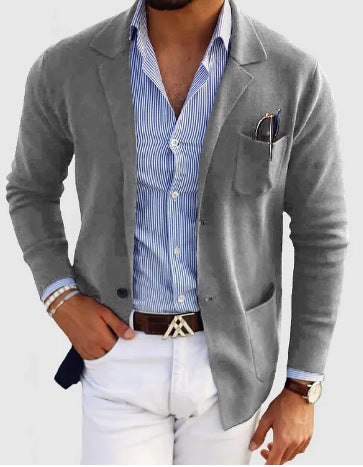 Man wearing a gray blazer over a blue striped shirt with white pants on a light gray background