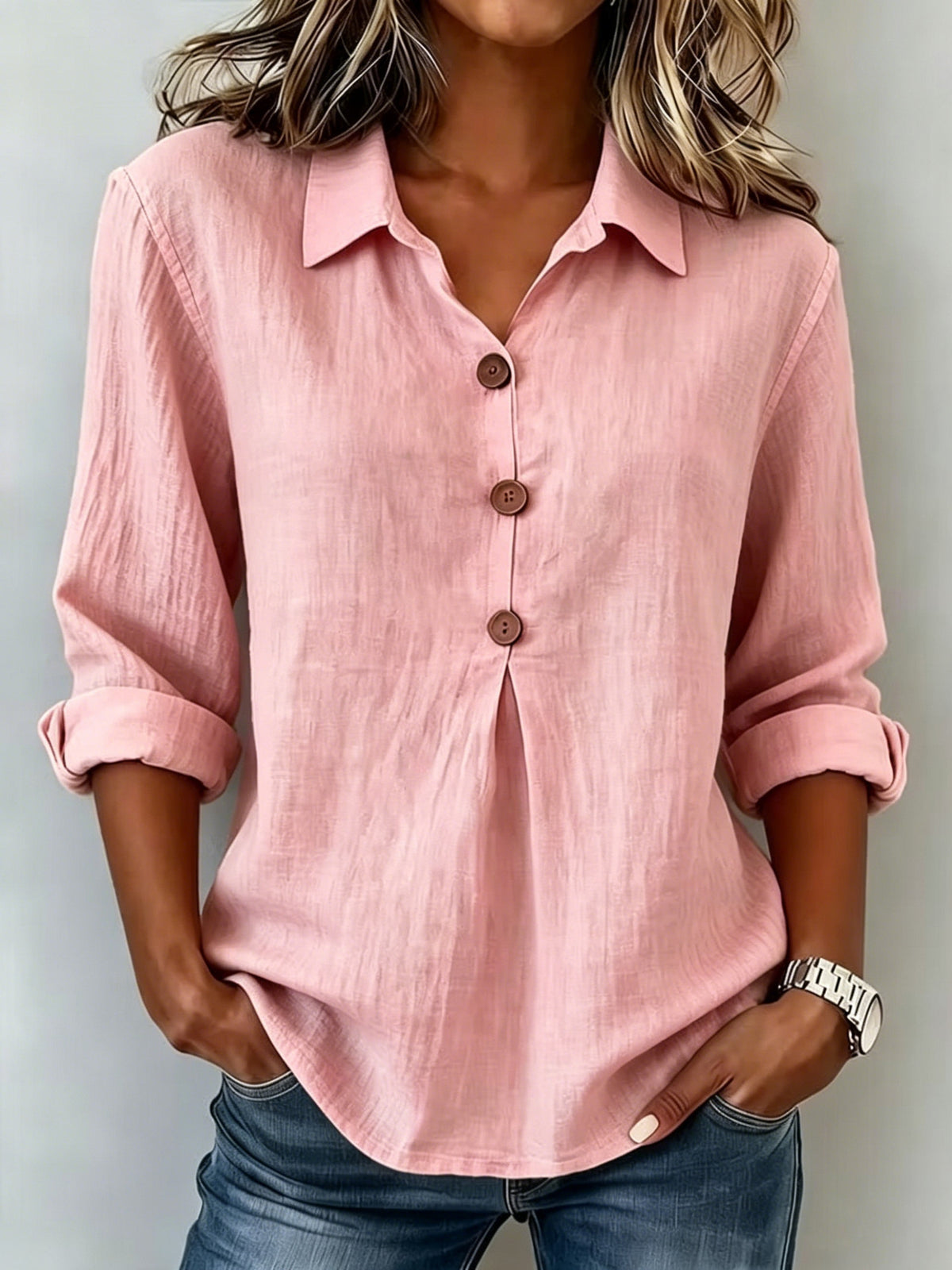 Person wearing a pink button-up shirt with rolled-up sleeves against a neutral background