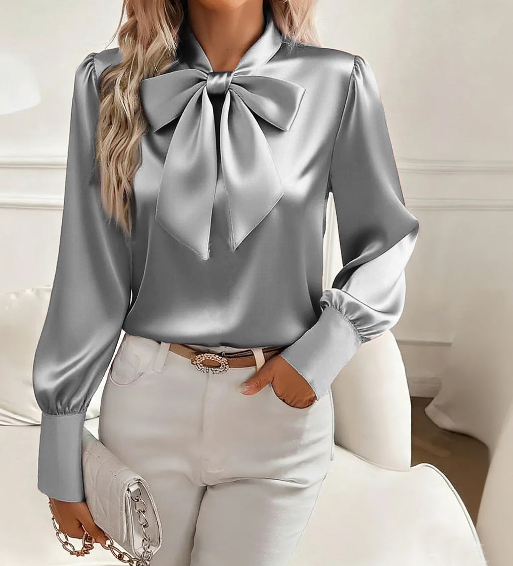 Person wearing a silver blouse with a large bow tie in a neutral setting