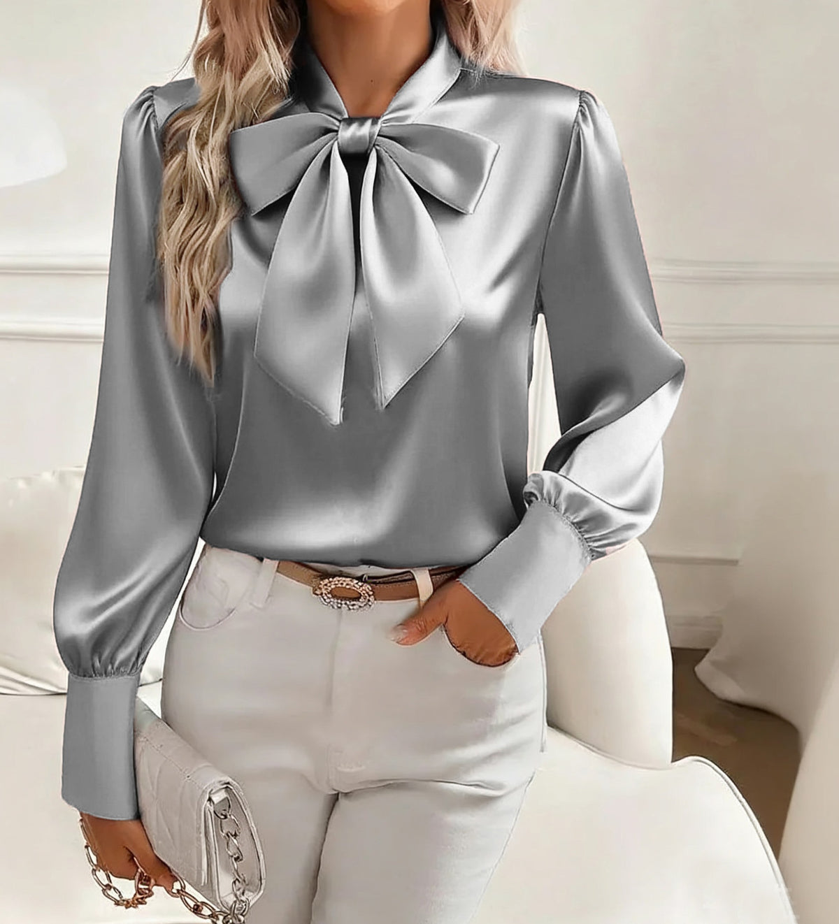 Person wearing a silver blouse with a large bow tie in a neutral setting