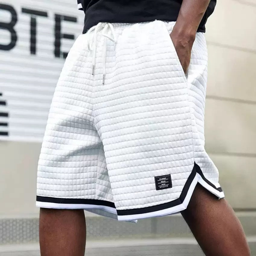 White quilted shorts with black trim worn by a person, with a blurred background.