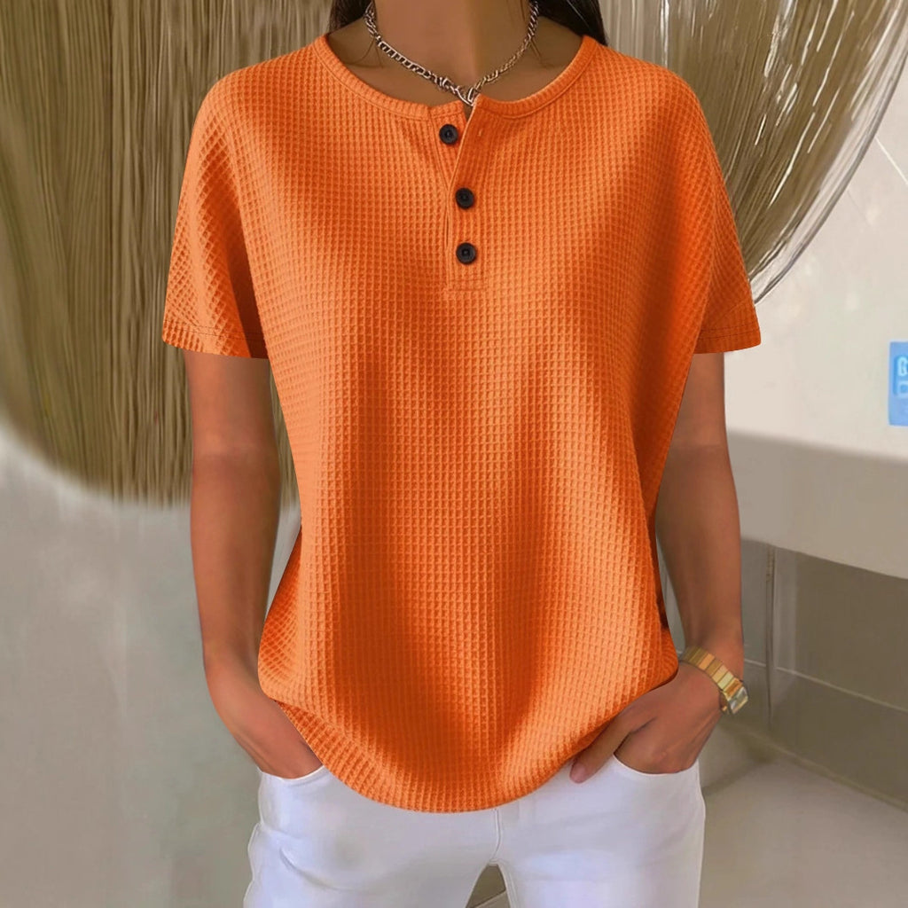 Person wearing an orange textured shirt with black buttons in a bathroom setting