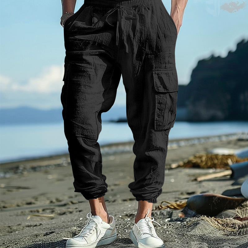 Person wearing black cargo pants and white sneakers on a beach with ocean and sky in the background