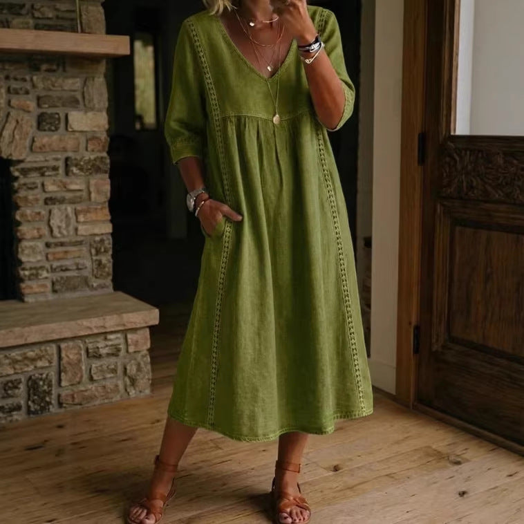 Woman wearing a green dress standing in a room with wooden floors and a stone fireplace.