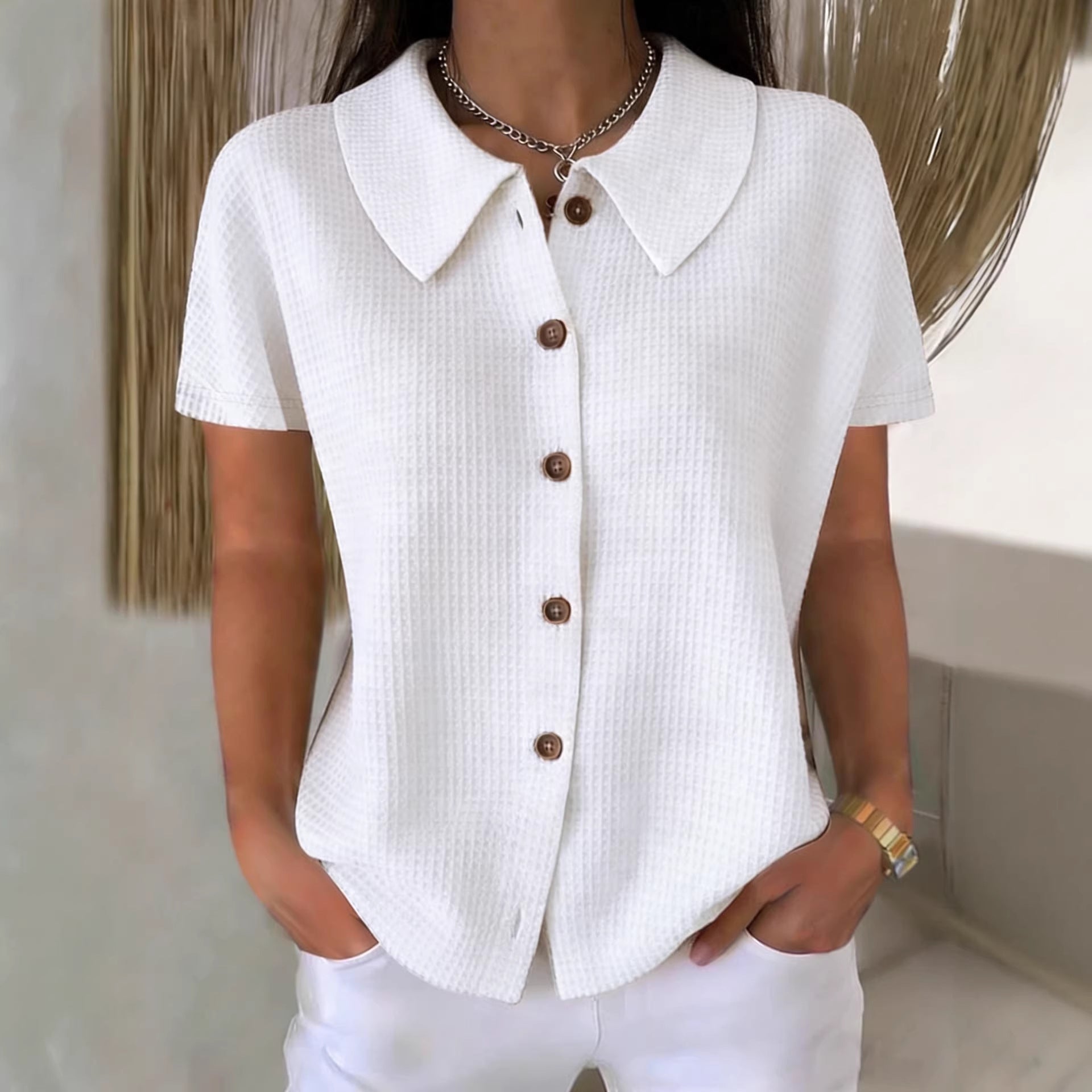 White textured shirt with brown buttons worn by a person, blurred background
