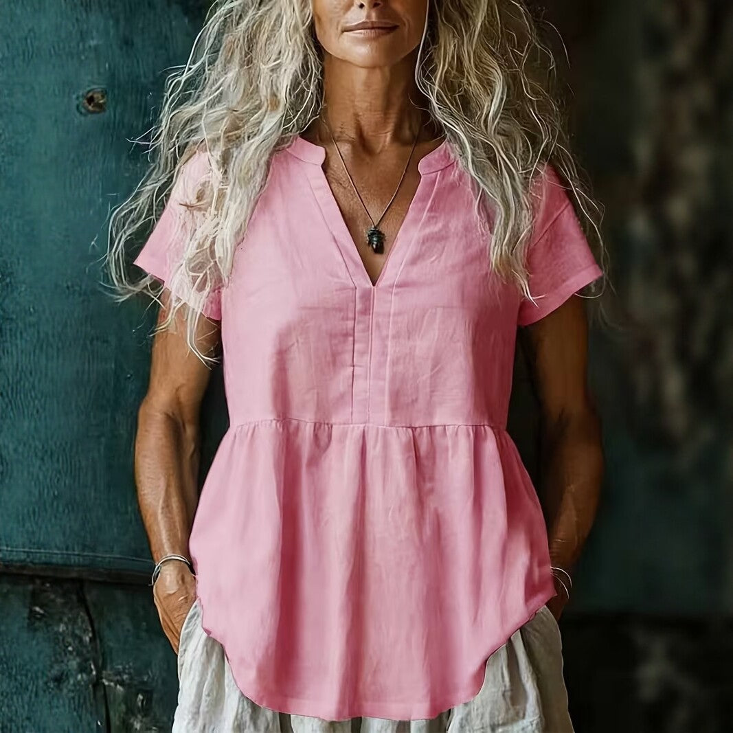 Woman wearing a pink linen top against a textured wall.