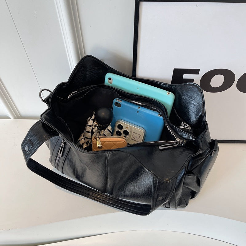 Black leather bag with items including a blue phone and keys on a white surface.