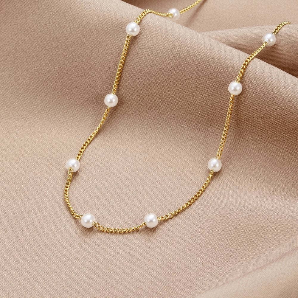 Gold chain necklace with pearls on a beige fabric background