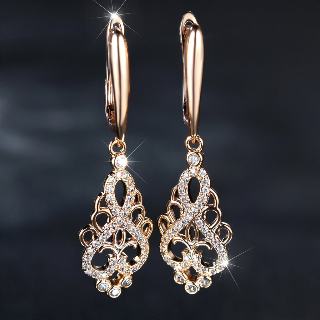 Rose gold earrings with intricate designs and sparkling stones on a dark background