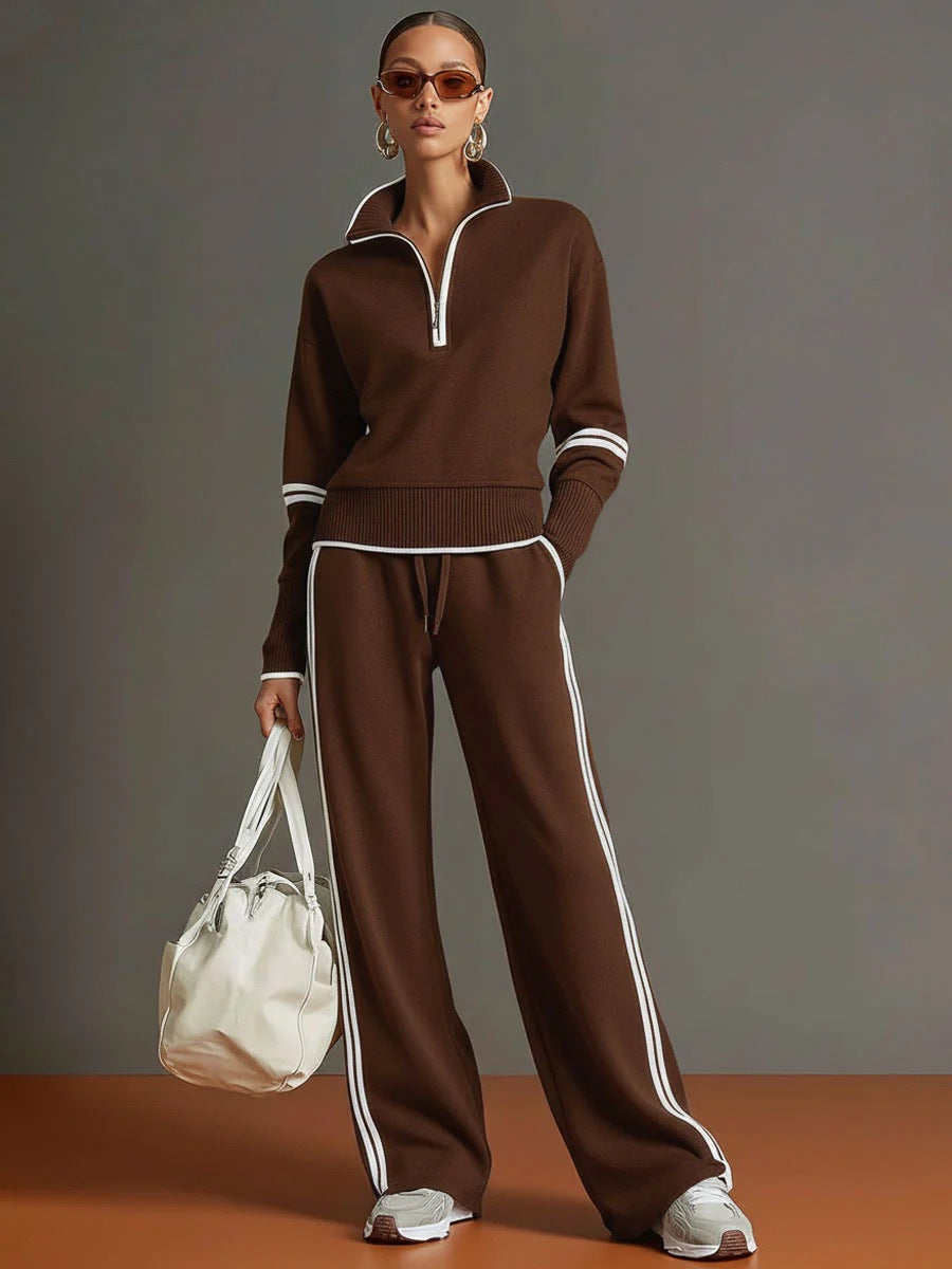 Woman wearing a brown tracksuit with white stripes, holding a white bag against a gray background.