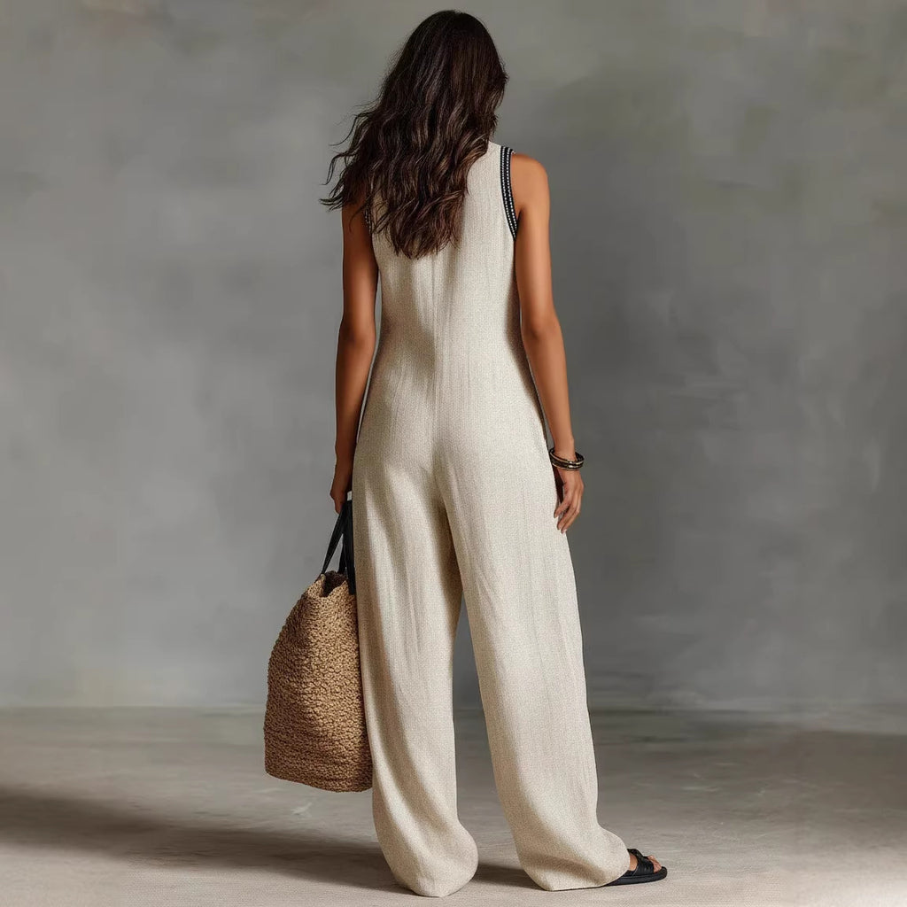 Woman in a beige jumpsuit holding a woven bag against a gray background