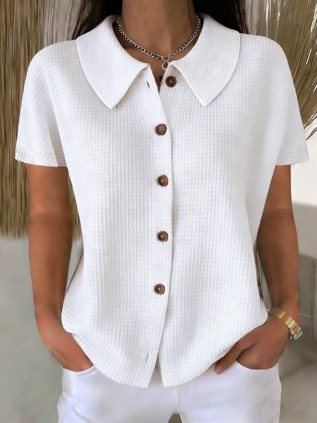 White textured shirt with brown buttons worn by a person indoors.