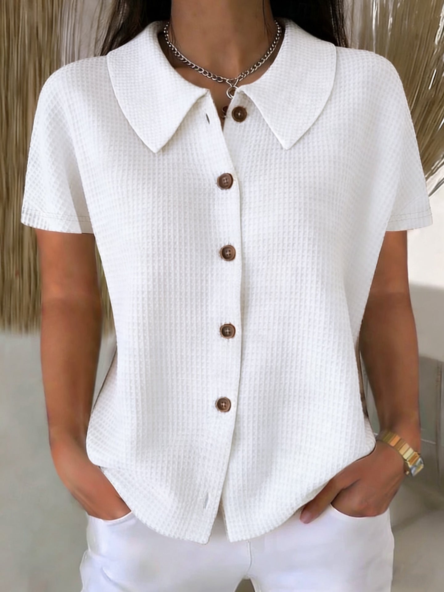 White textured shirt with brown buttons worn by a person indoors.