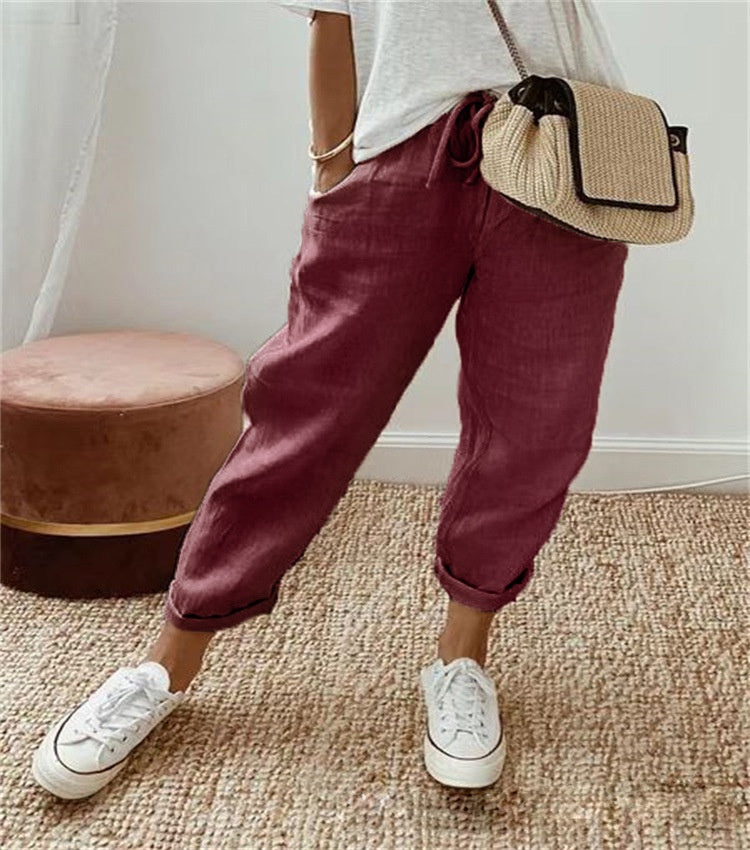 Person wearing maroon pants, white shirt, and white sneakers with a straw bag indoors.
