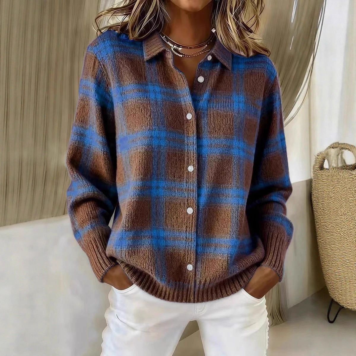 Person wearing a brown and blue plaid sweater with white pants in a neutral setting.