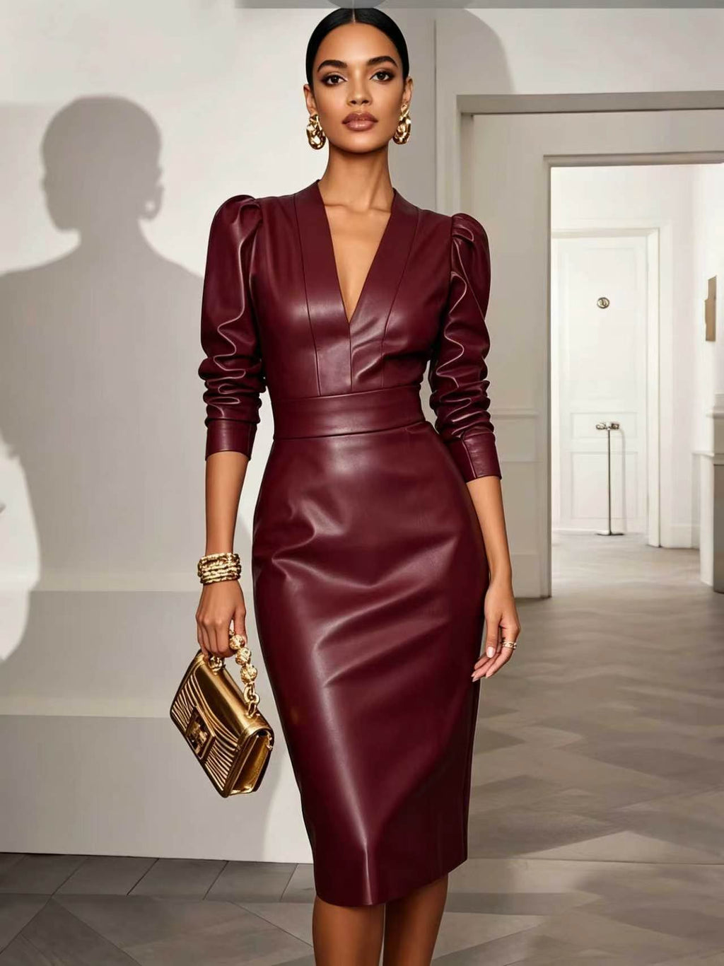 A woman models a deep burgundy faux-leather midi dress with puffed three-quarter sleeves and a deep V-neckline, holding a gold metallic clutch in a bright, modern hallway.