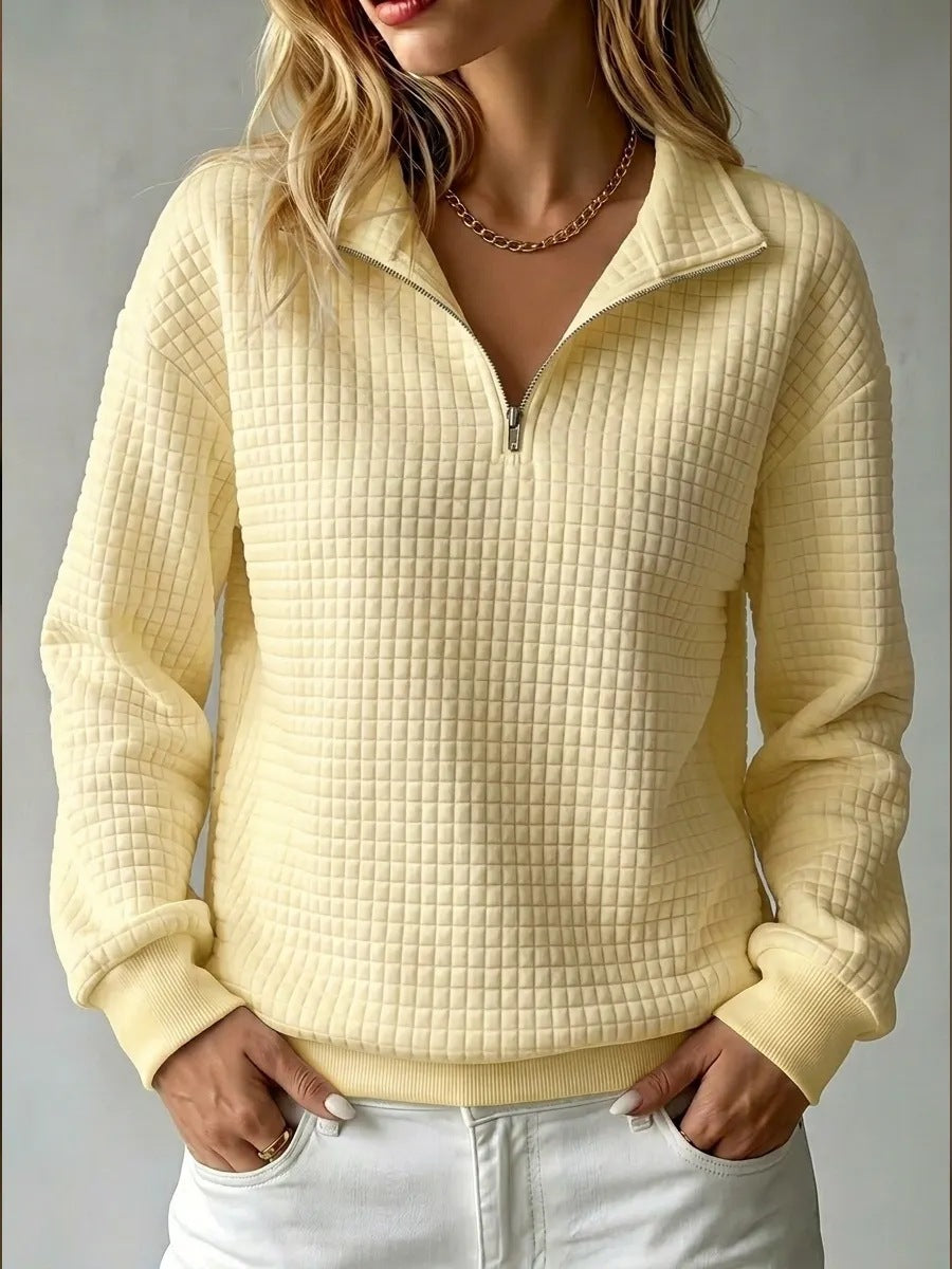 A woman wearing a pale yellow waffle-knit quarter-zip pullover sweater with a stand collar, paired with white pants, shown against a neutral gray background.