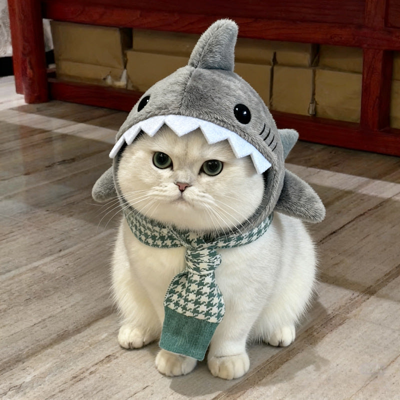 Cat wearing a shark costume with a hood and a scarf on a wooden floor.