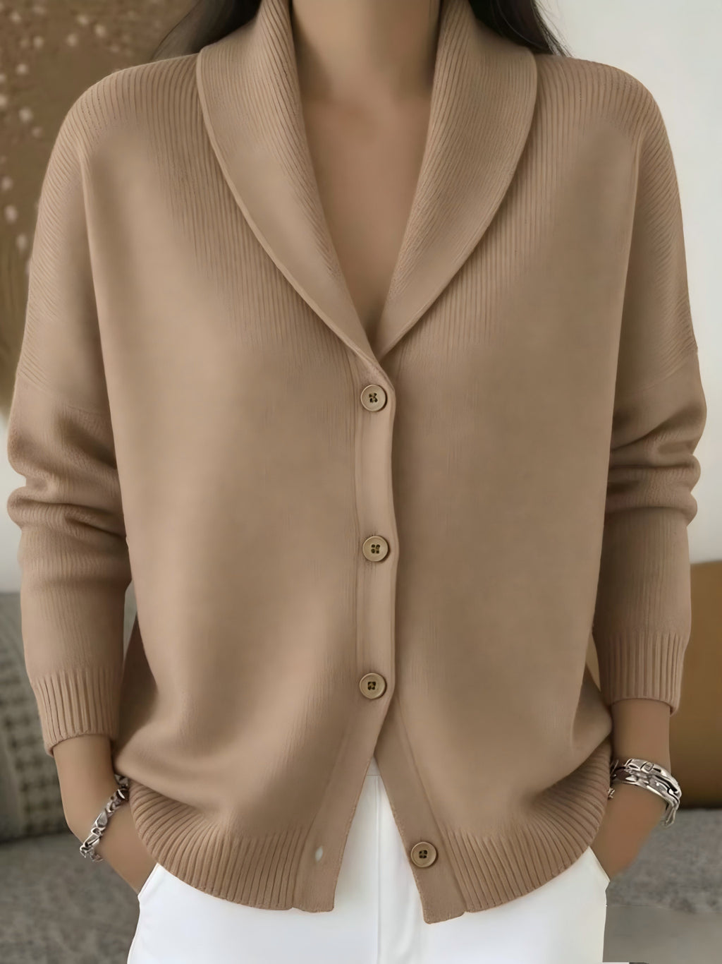 A woman wearing a beige ribbed knit cardigan sweater with a shawl collar and front buttons, paired with white pants.
