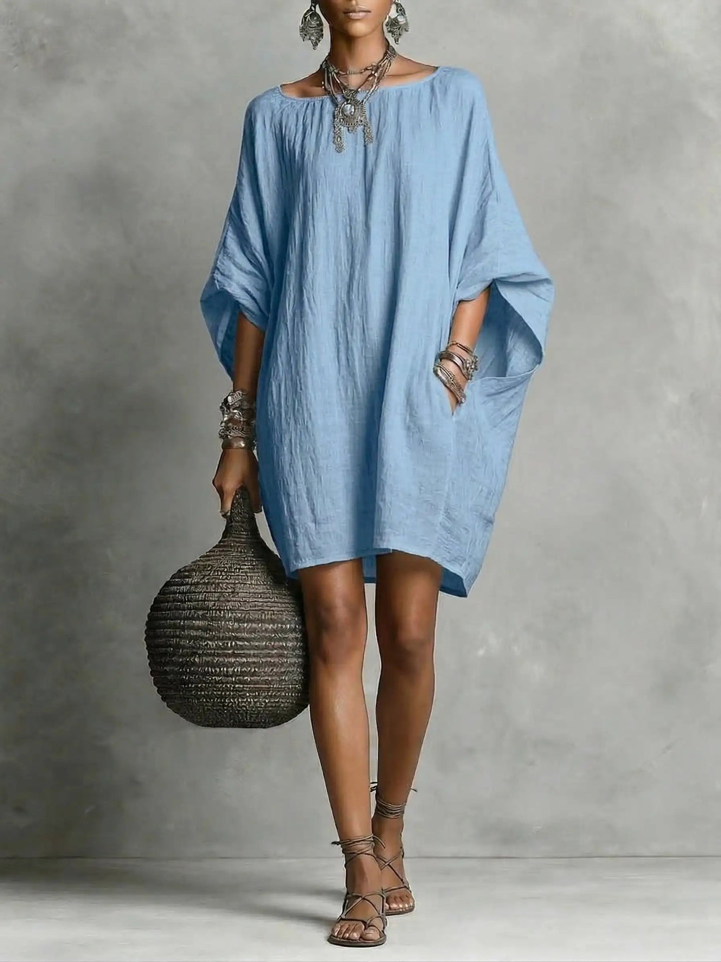 Woman wearing a blue dress holding a woven bag against a gray background