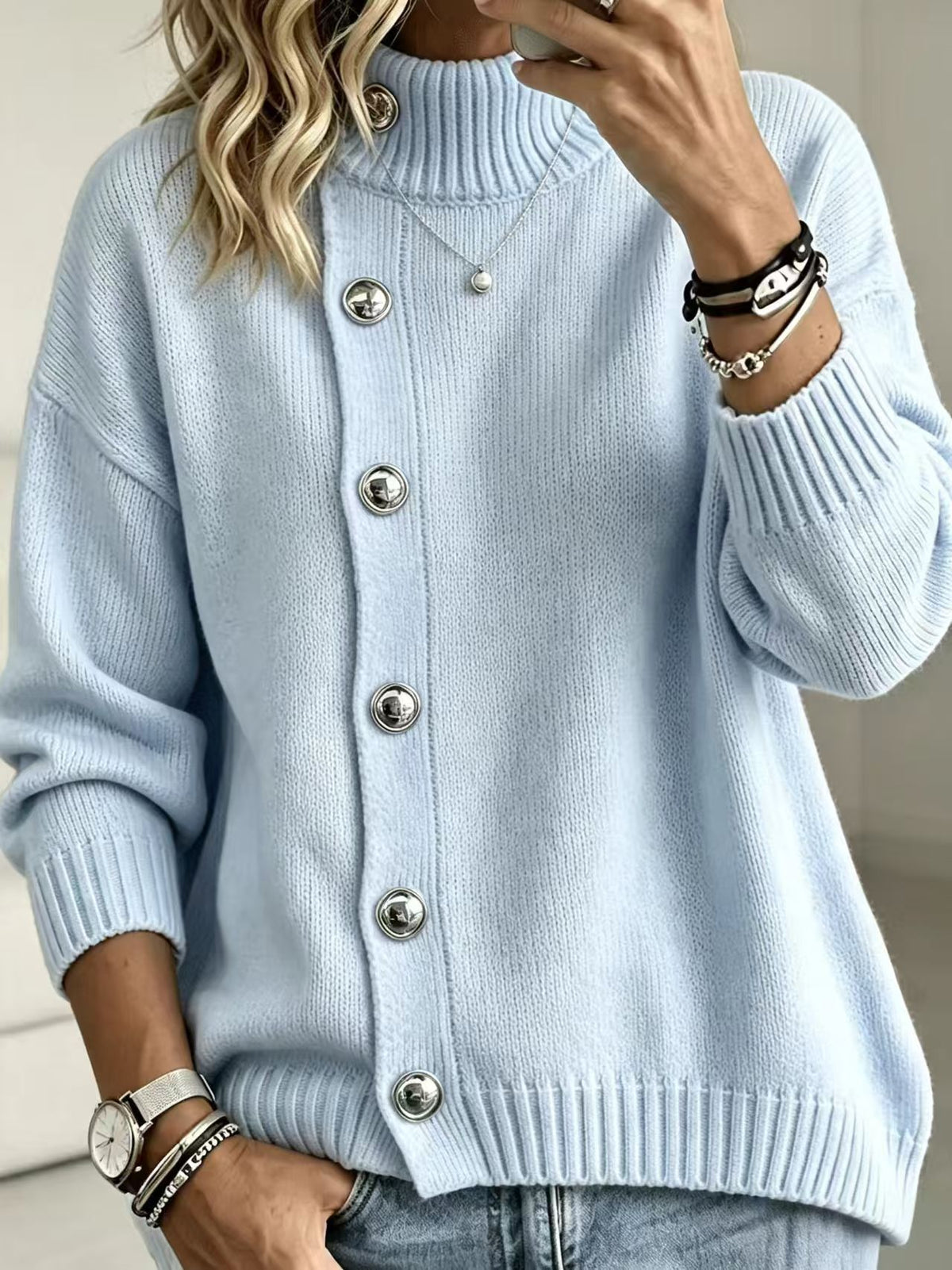 A woman wearing a light blue ribbed knit cardigan sweater with large silver buttons, paired with light blue jeans and accessorized with bracelets and a necklace.