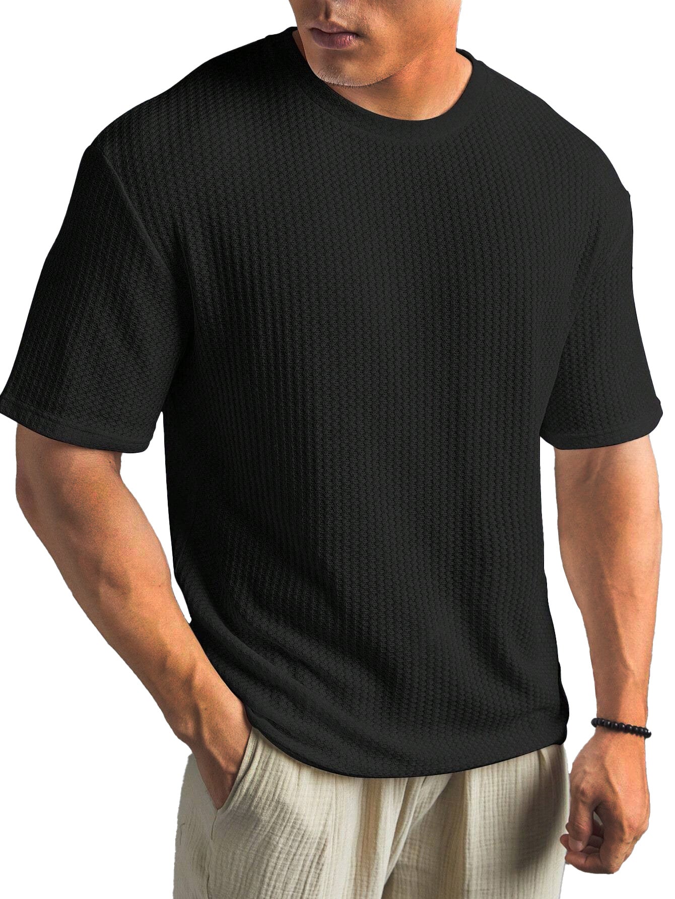 Man wearing a black ribbed t-shirt and light-colored pants on a white background