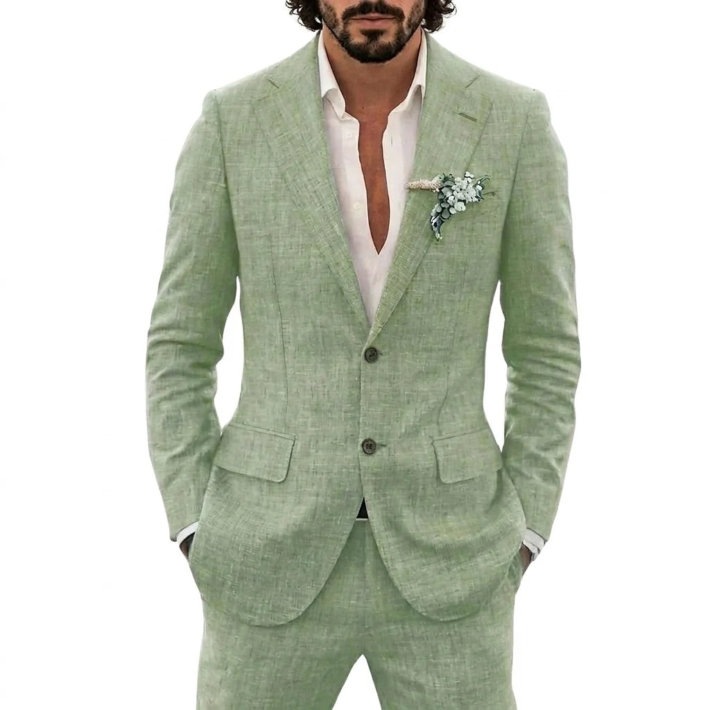 A man wearing a light sage green textured linen suit jacket and matching trousers, styled with an open white dress shirt and a green floral boutonniere, against a solid white background.