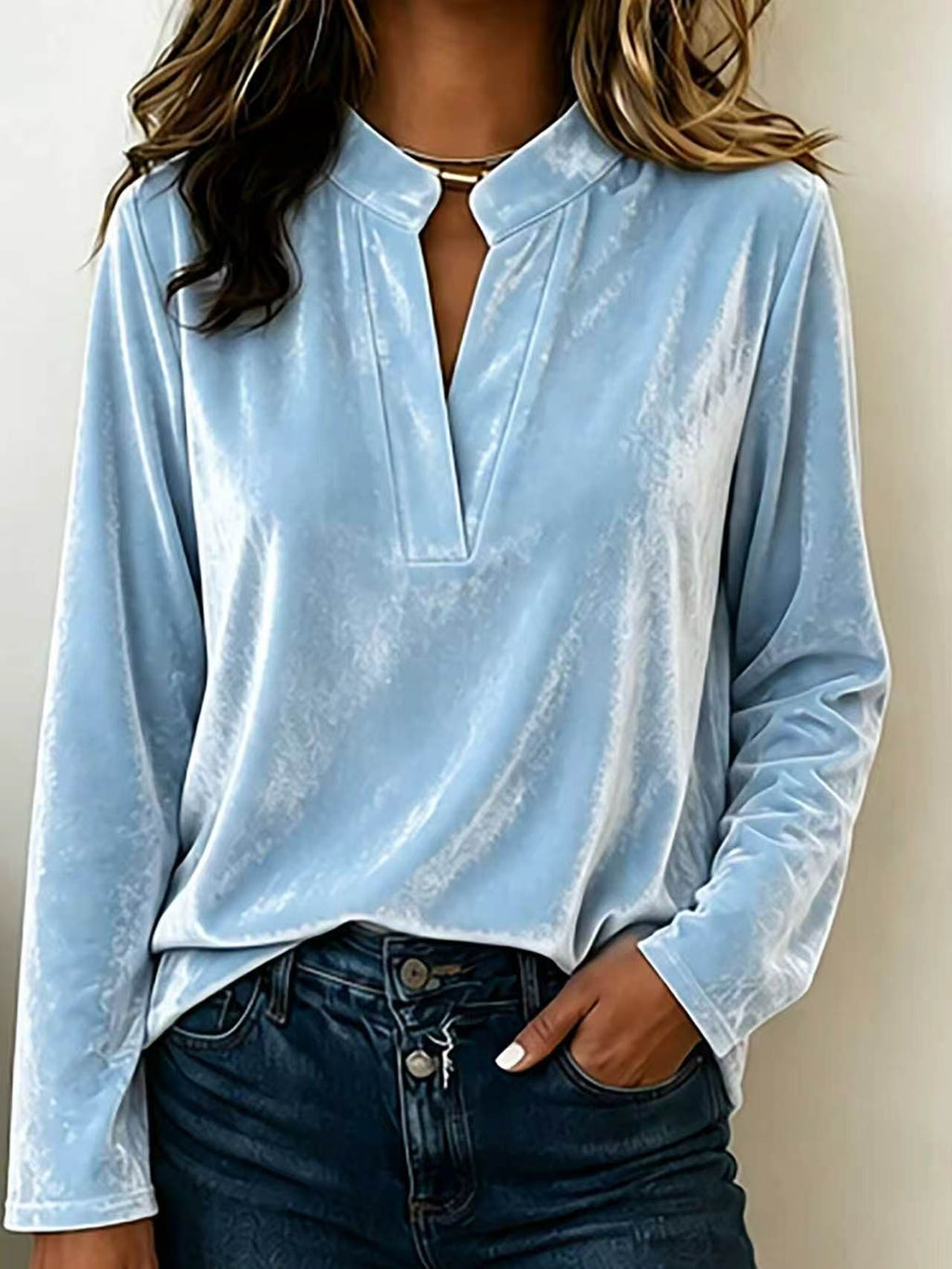 A woman wearing a light blue long-sleeve velvet top with a split V-neckline and dark blue jeans, shown from the shoulders to the hips against a plain light background.