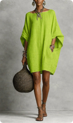 Woman wearing a bright green dress holding a woven bag against a gray background