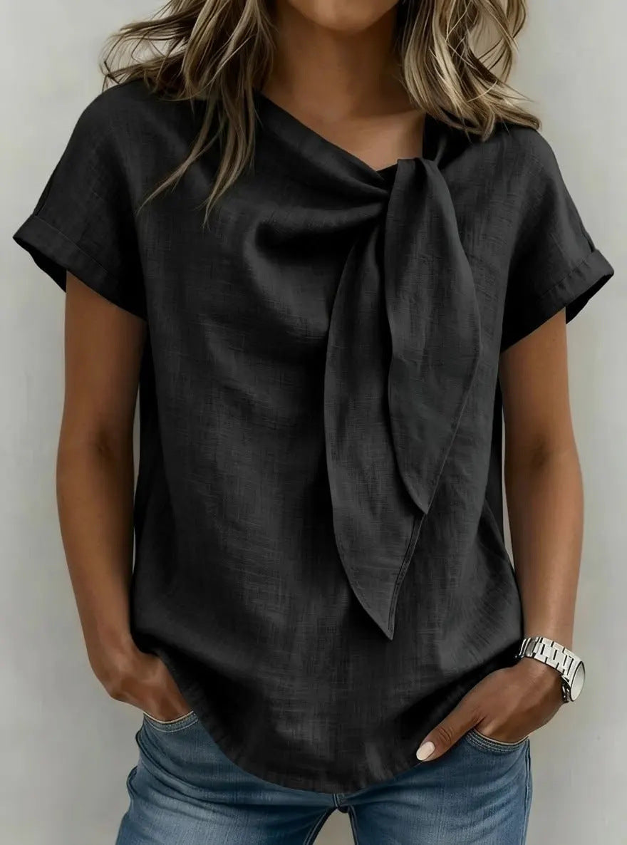 Woman wearing a black top with a bow detail and blue jeans against a neutral background