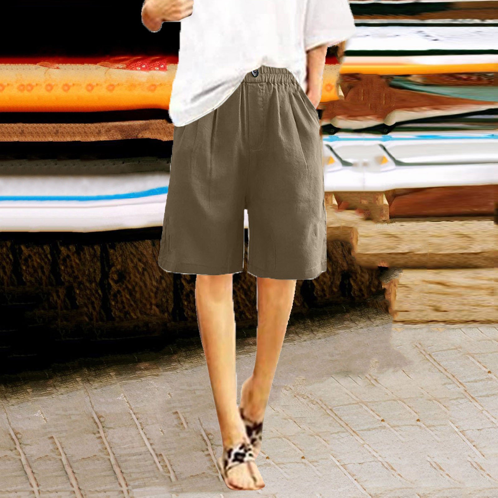 Person wearing brown shorts standing on a paved surface with stacked wooden planks and surfboards in the background.