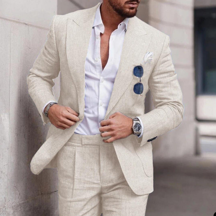 Man wearing a beige suit with a white shirt, standing against a blurred background.