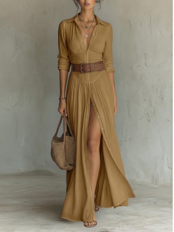 Woman wearing a long brown dress with a belt, holding a bag against a plain background