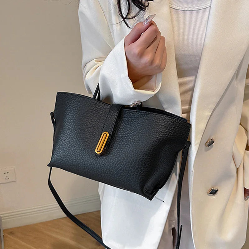 Person holding a black handbag with a gold clasp indoors.