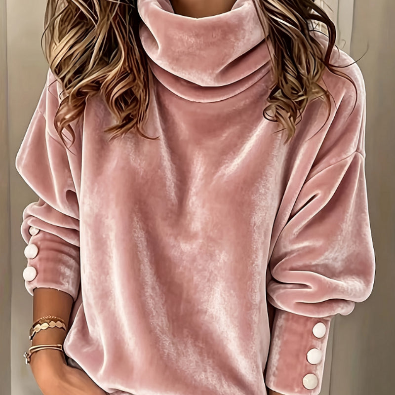 A person wearing a dusty pink velvet turtleneck sweatshirt with white decorative buttons on the sleeves, shown from the neck down against a neutral indoor background.