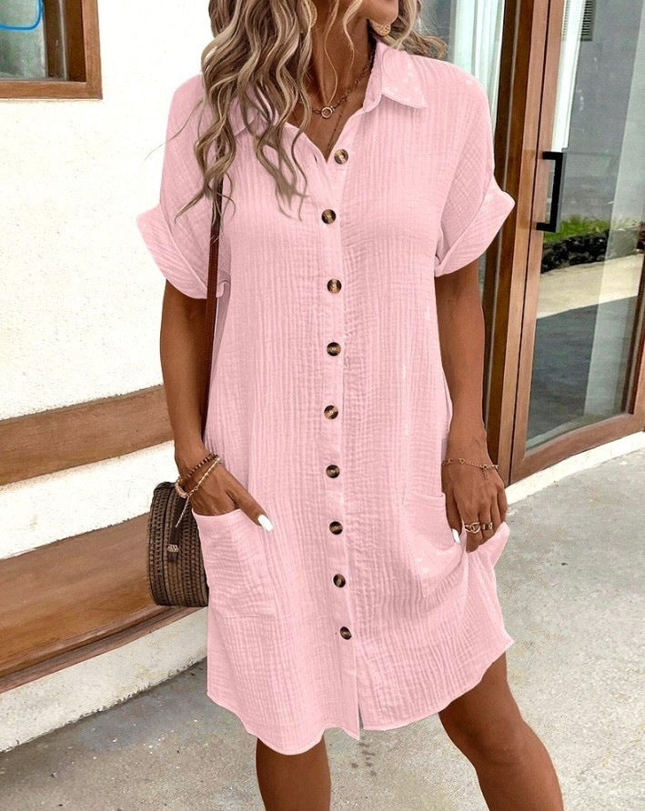Woman wearing a pink button-up dress standing outdoors.