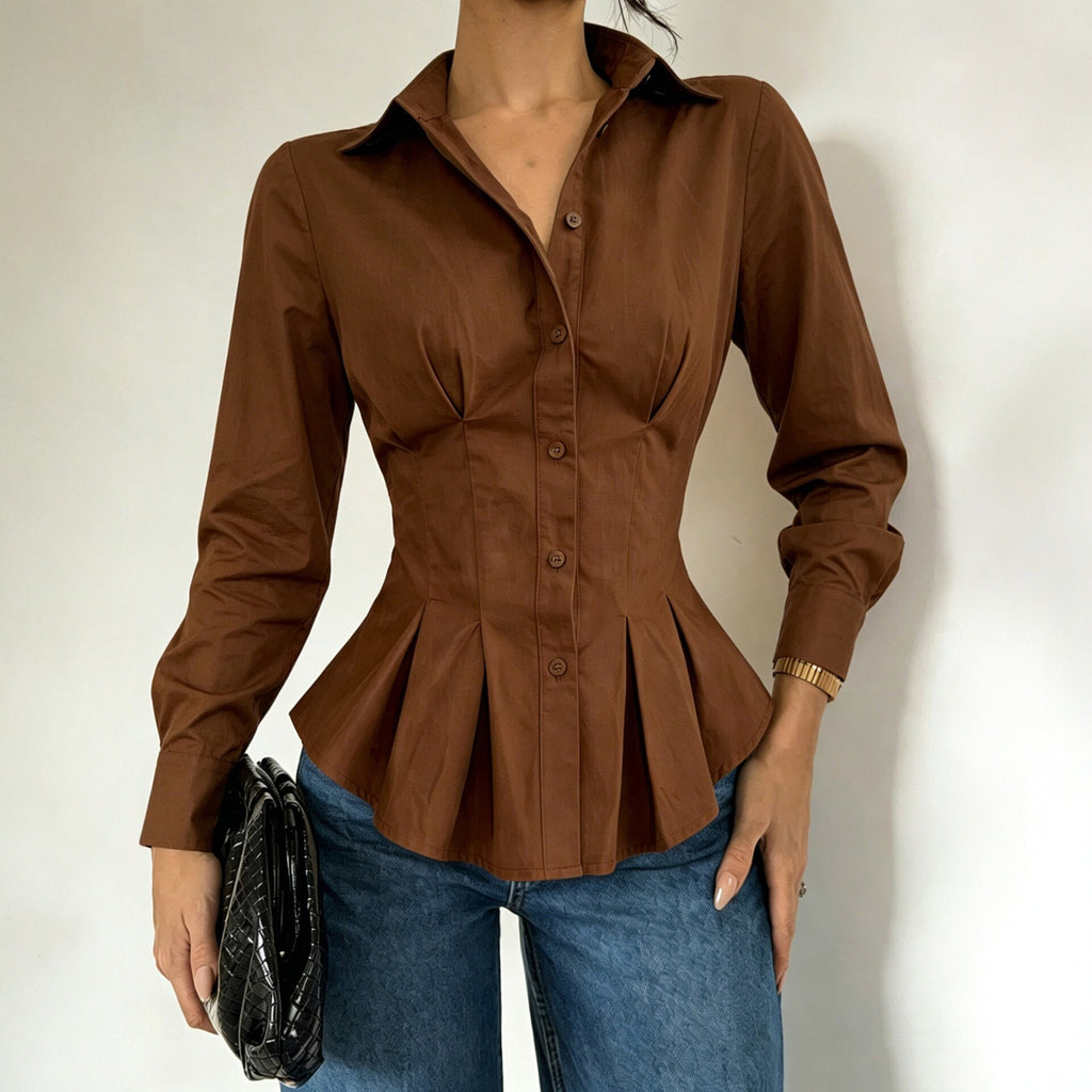 A woman wearing a fitted long-sleeve brown button-front blouse with a peplum hem, paired with blue jeans and holding a black clutch against a plain light background.