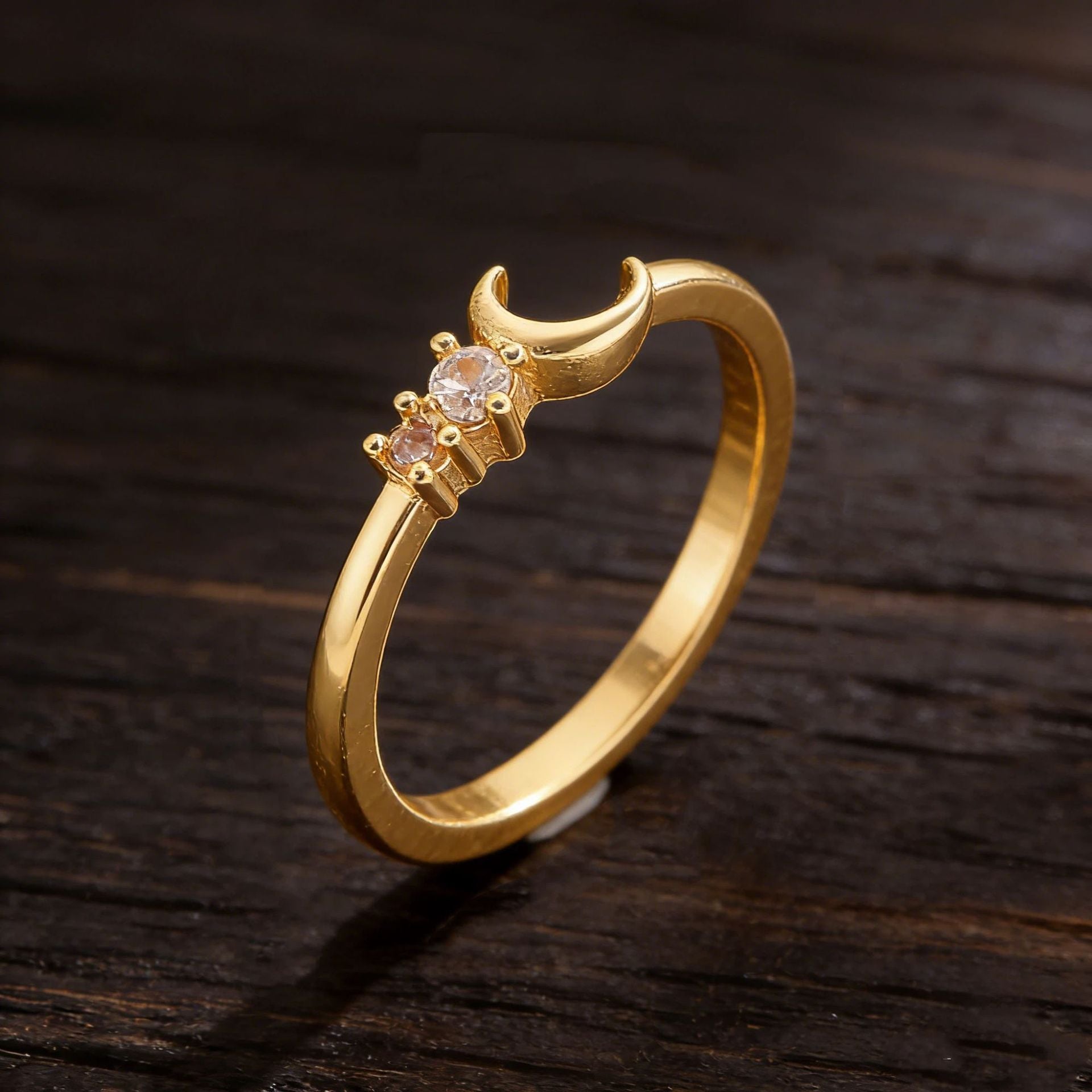 Gold ring with a moon design and embedded stones on a dark wooden surface