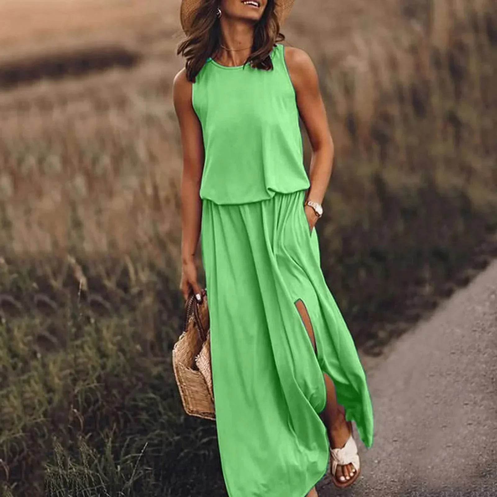 Woman in sleeveless green maxi dress with side slit, straw hat, and bag, walking outdoors