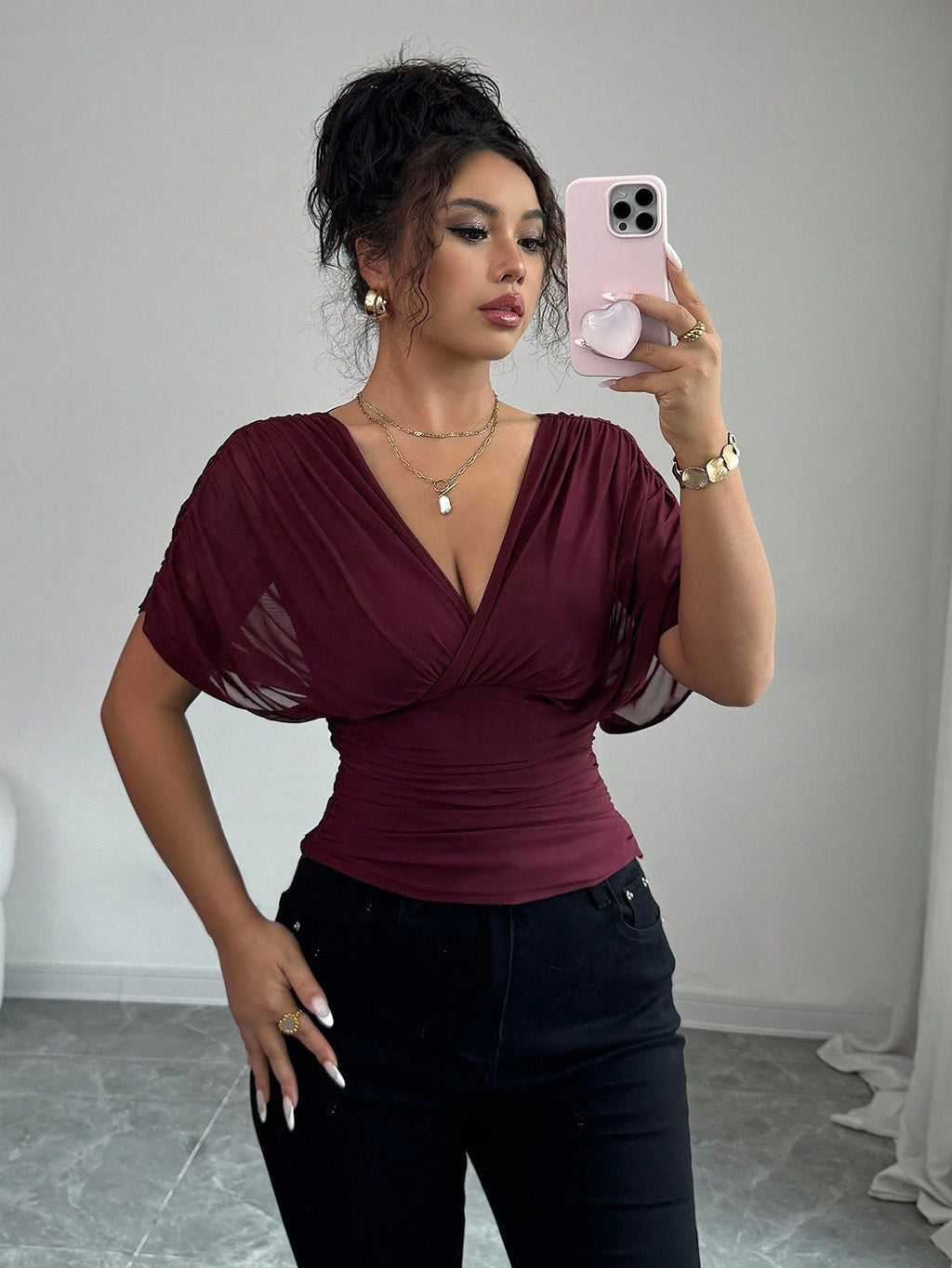 Woman taking a mirror selfie wearing a burgundy top and black pants.