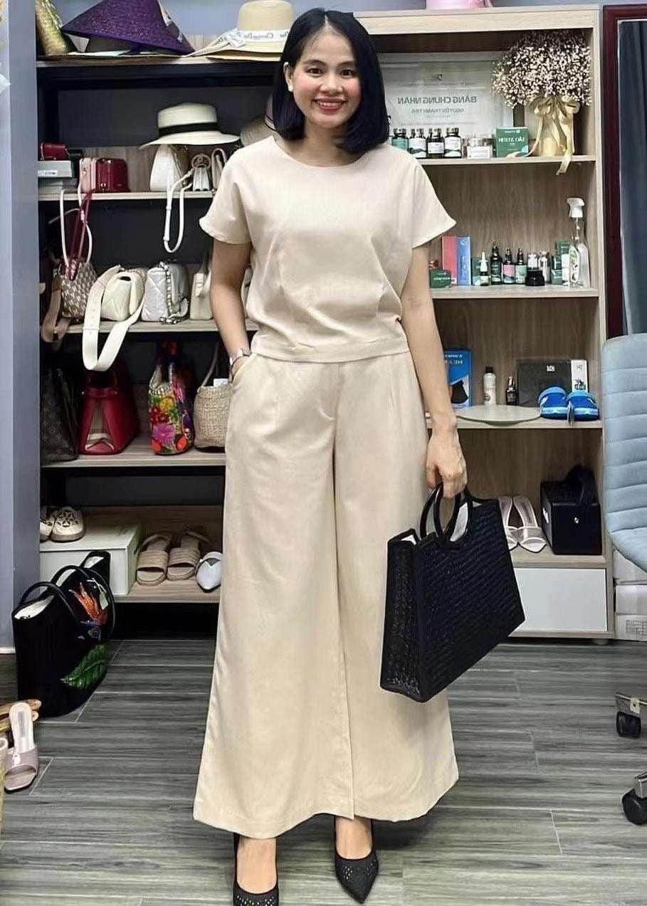 Woman in beige wide-leg jumpsuit holding black tote bag, standing in chic boutique