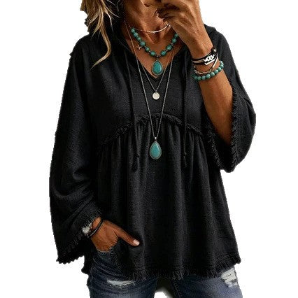 A woman wearing a loose black long-sleeve top with frayed edges, layered necklaces, and turquoise jewelry, paired with blue jeans, shown against a plain white background.