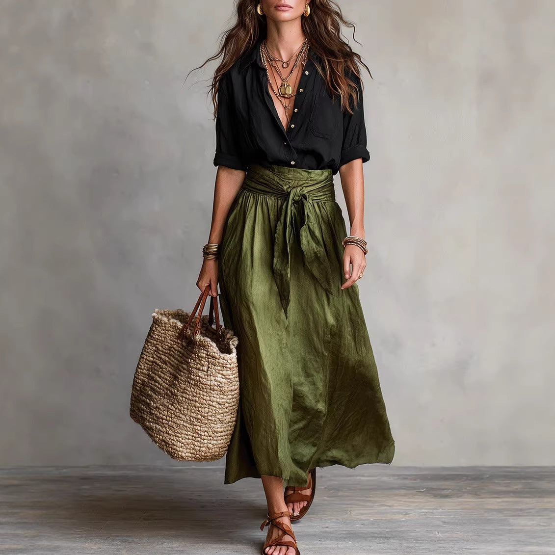 Woman wearing a black top and green skirt holding a woven bag against a gray background