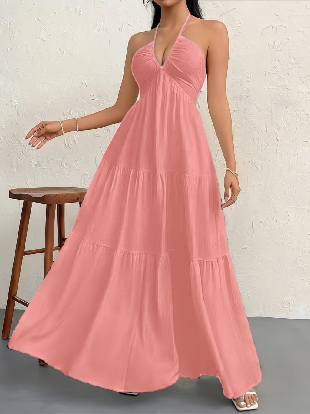 Woman wearing a pink halter neck dress against a white brick wall.
