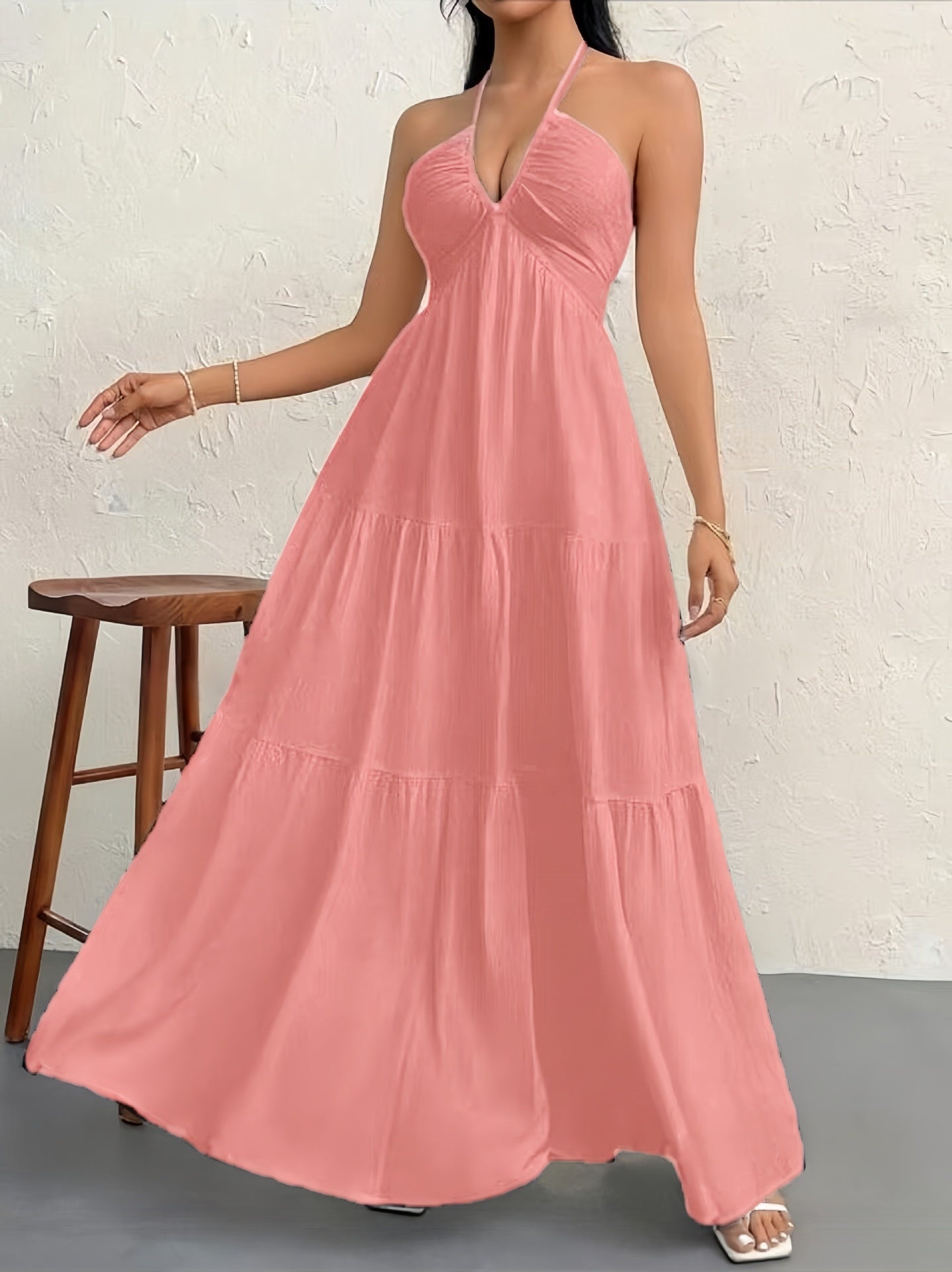 Woman wearing a pink halter neck dress against a white brick wall.