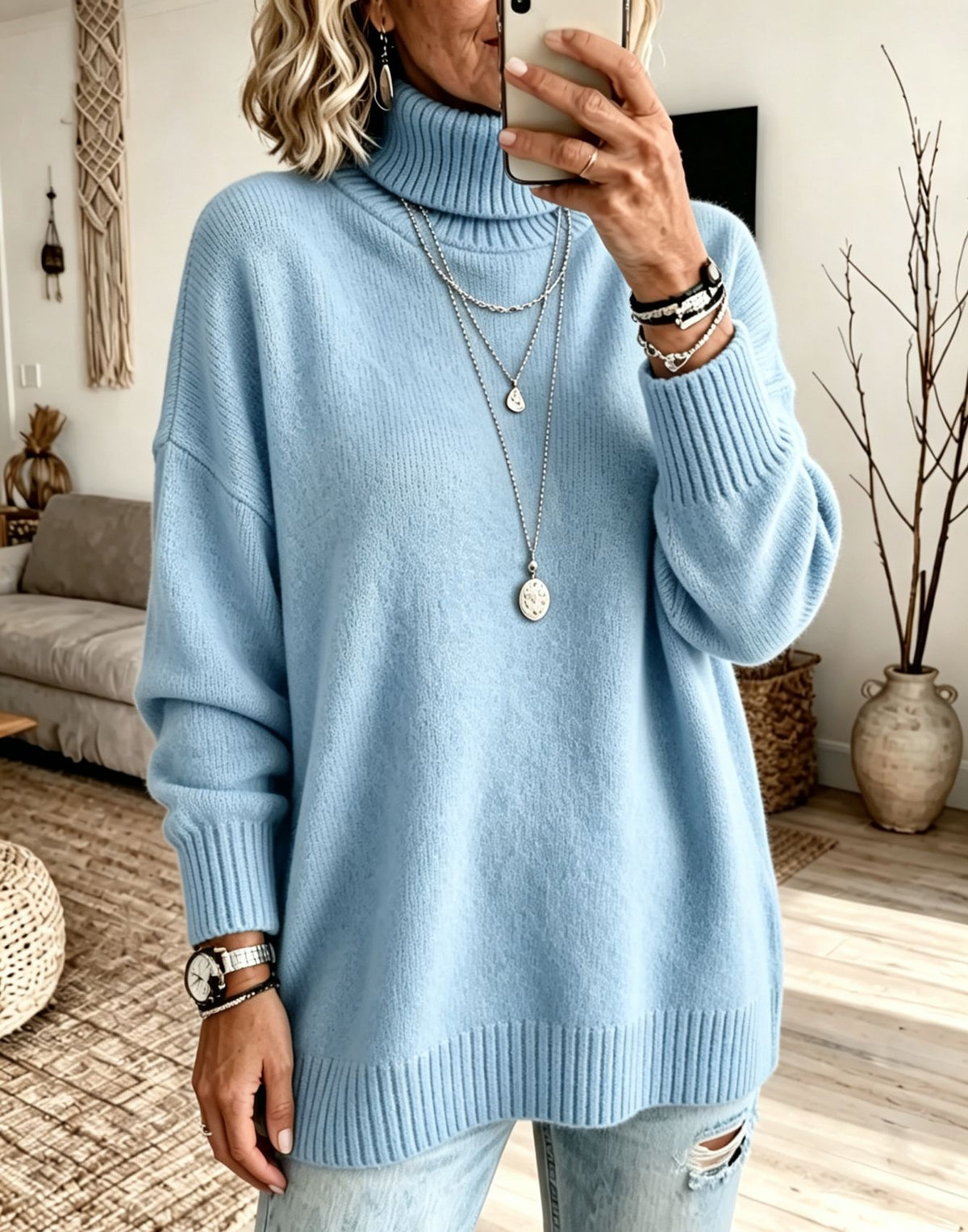 A woman takes a mirror selfie wearing a light blue ribbed turtleneck sweater and light-wash distressed jeans in a cozy living room setting.
