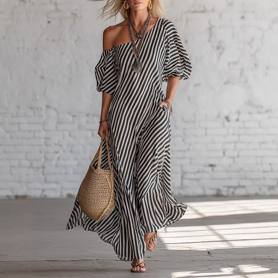 Woman wearing a black and white striped dress holding a woven bag against a white brick wall.