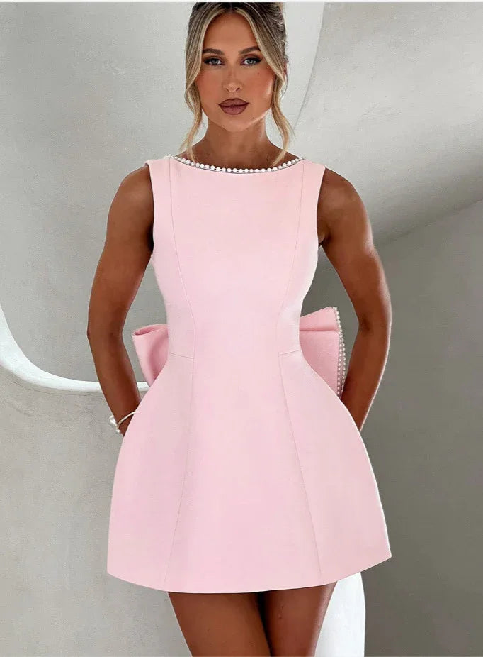 Woman wearing a pink dress with pearl embellishments against a neutral background