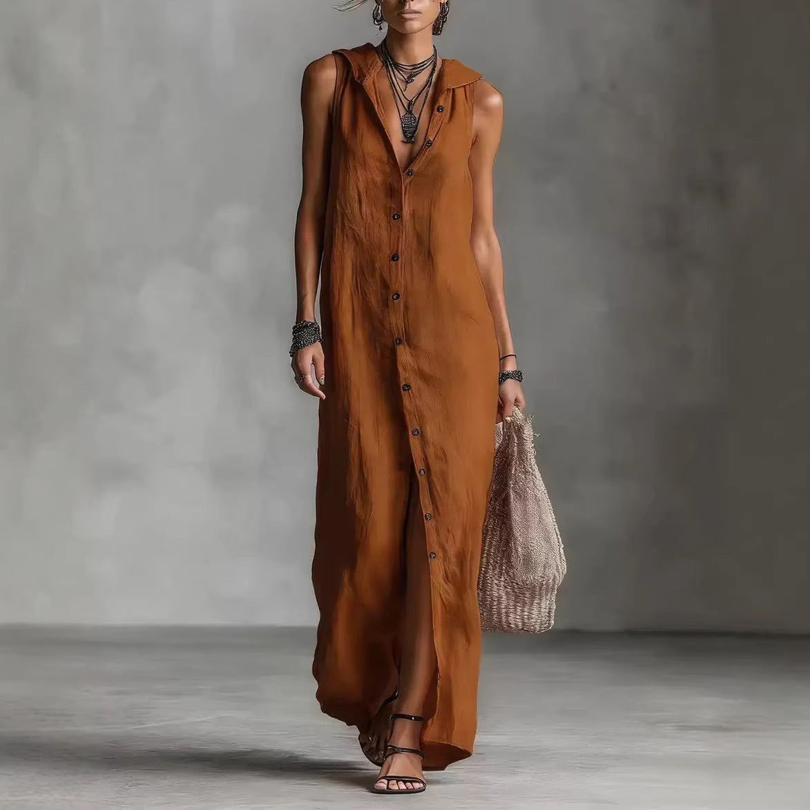 Woman wearing a long brown dress holding a woven bag against a gray background
